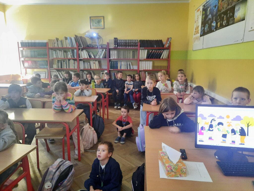 Dzieci siedzą w ławkach i oglądają lekcję online