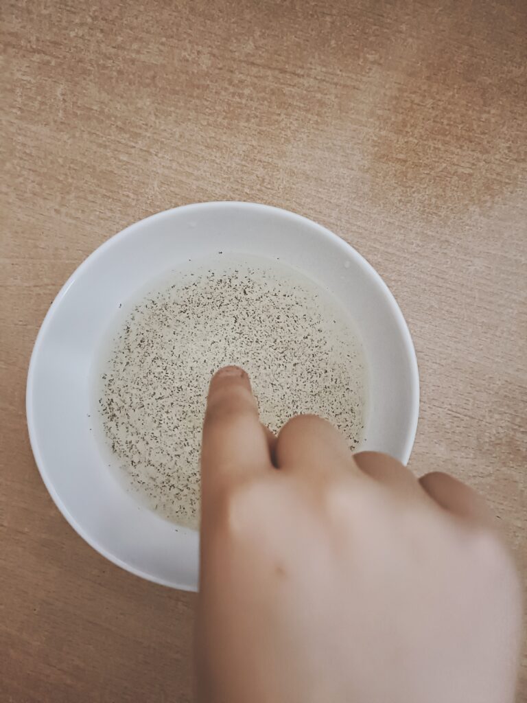 palec ucznia zamoczony w misce z wodą posypaną pieprzem w doświadczeniu pokazującym dlaczego należy myć ręce wodą z mydłem